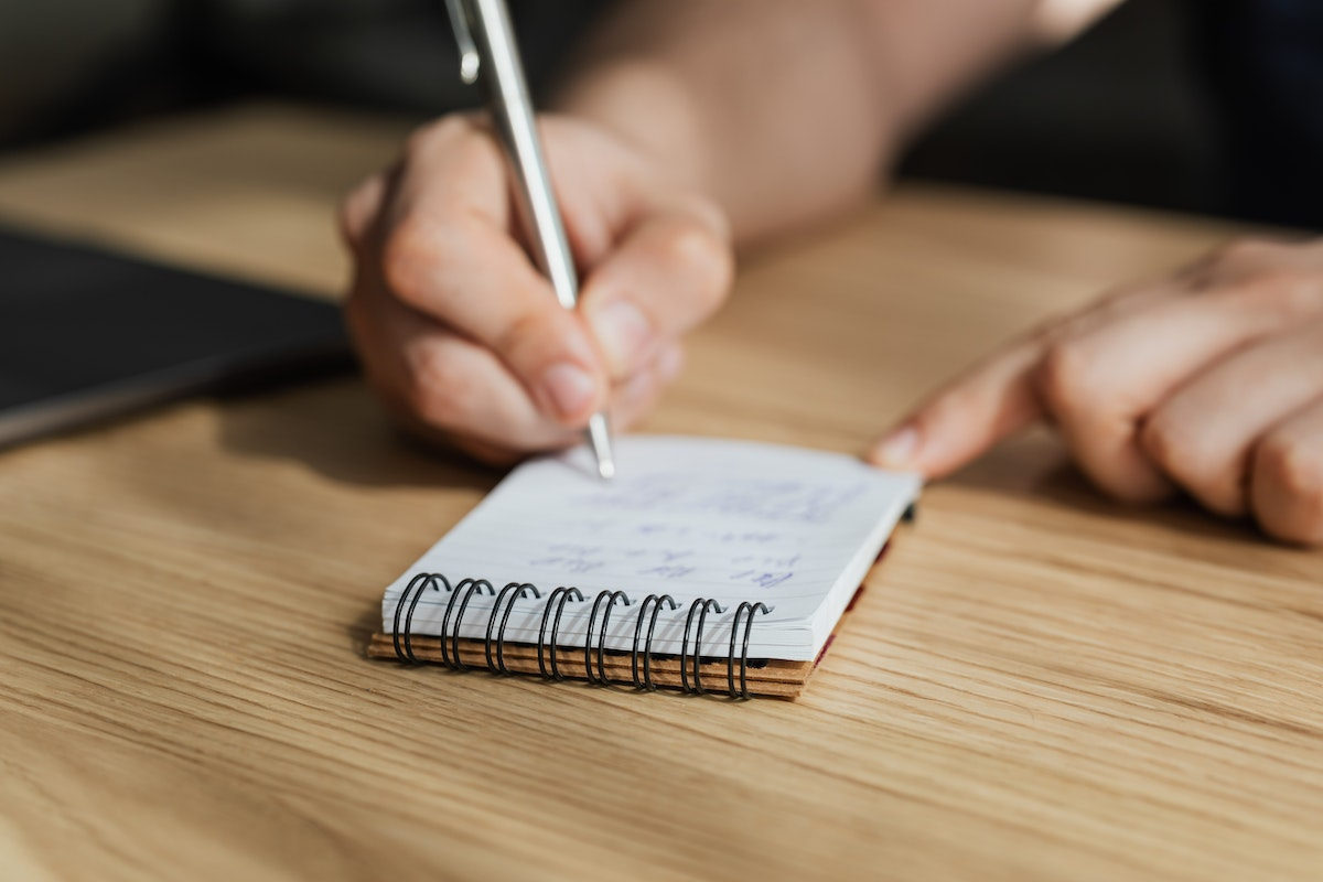 Concurso PM MG (CFO): A imagem mostra uma pessoa anotando em uma caderneta umas informações
